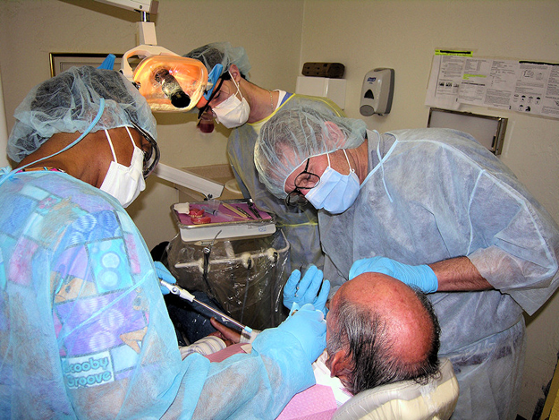 Paul Burtner, DMD, standing right, carefully cleans a patient's denture surface. Dental assistant Carrie Hines, left, and UF dental student Evan Rosen, second from left, are essential team members ensuring dental services for patients with disabilities. Dr. Burtner is the founder of the Tacachale Dental Clinic's community pilot program